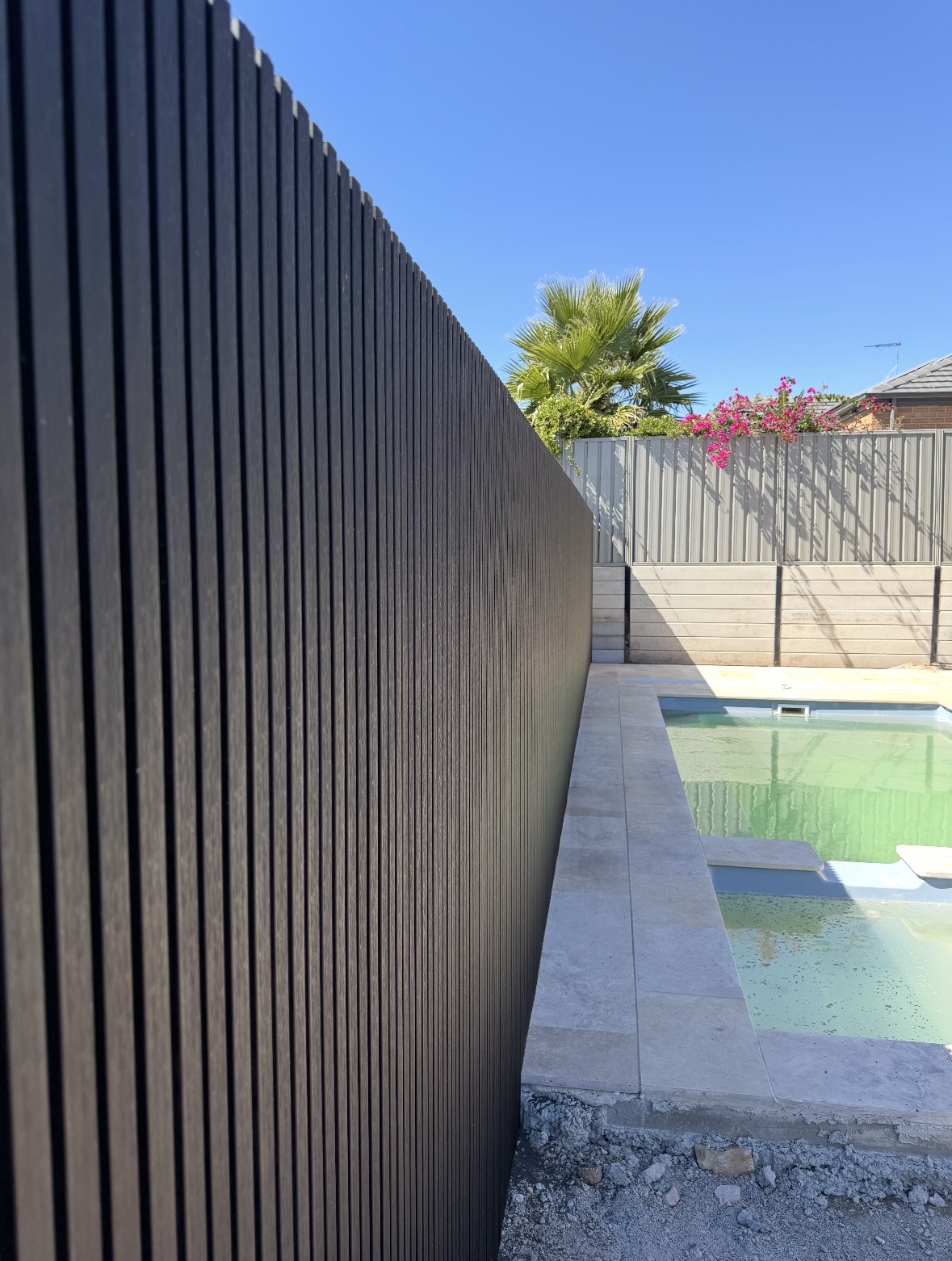 Black slat fencing beside a pool and flowering garden